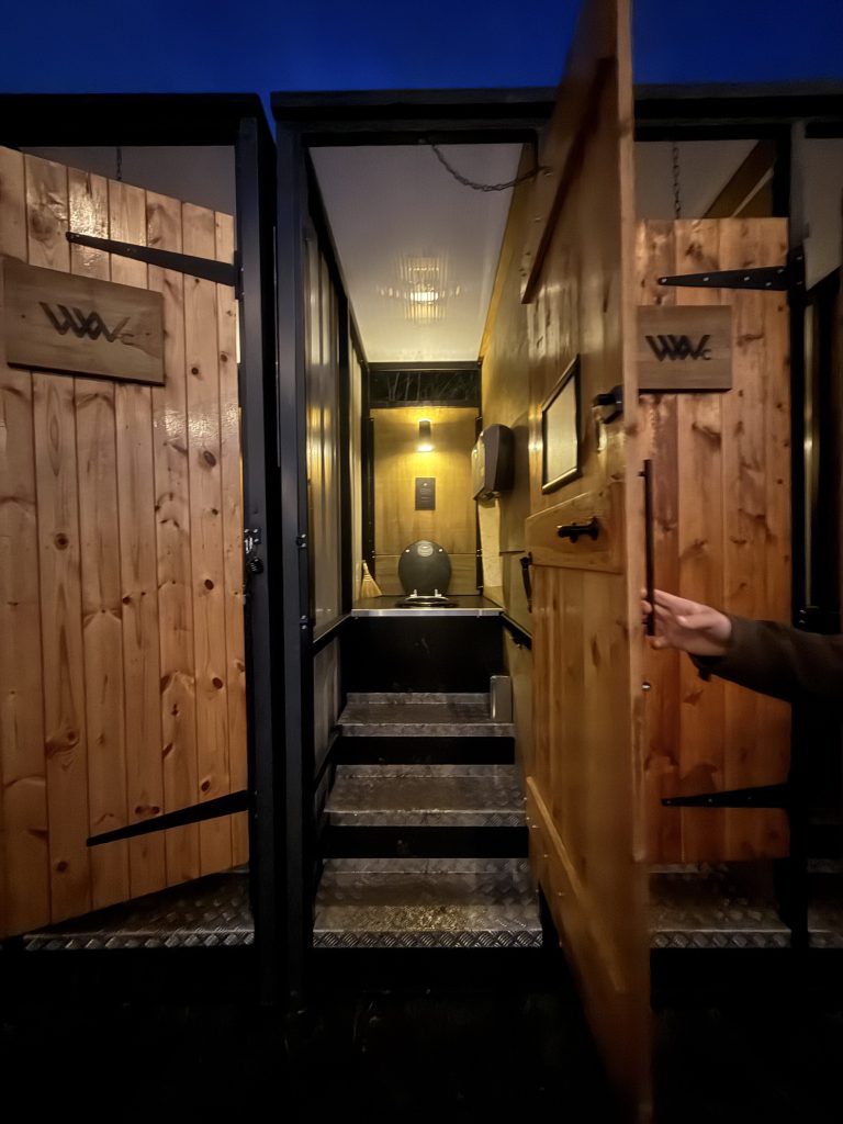 Entrance to a modern restroom facility with wooden doors and steps leading to a well-lit interior.